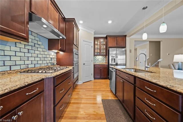 kitchen featuring light wood finished floors, a sink, hanging light fixtures, appliances with stainless steel finishes, and under cabinet range hood