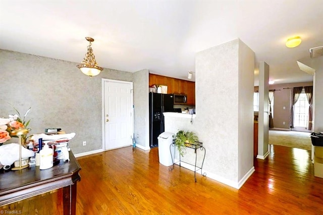 kitchen with black fridge with ice dispenser, wood finished floors, baseboards, stainless steel microwave, and brown cabinets