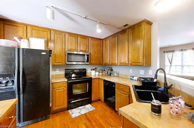 kitchen featuring light wood-style floors, a sink, brown cabinets, and black appliances