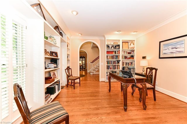 office featuring built in shelves, baseboards, arched walkways, ornamental molding, and light wood-type flooring