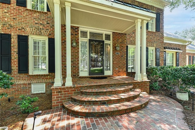 view of exterior entry with brick siding and covered porch