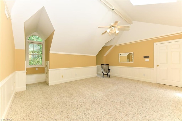 additional living space with a wainscoted wall, carpet flooring, vaulted ceiling with beams, and a ceiling fan