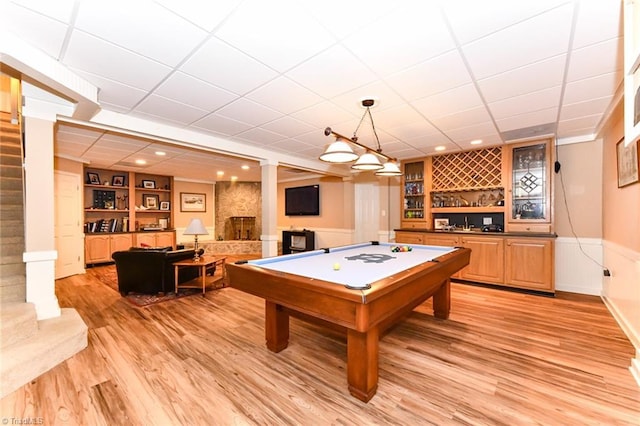 rec room featuring light wood finished floors, built in features, a drop ceiling, a wainscoted wall, and billiards