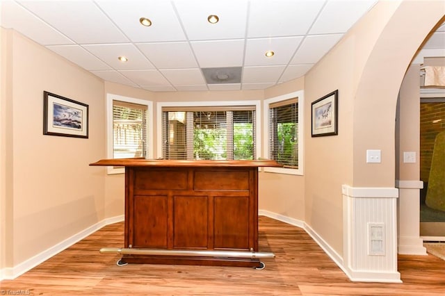 bar featuring arched walkways, light wood-type flooring, and baseboards