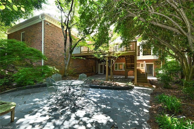 view of patio with a wooden deck, outdoor dining space, and stairs