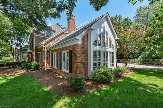 view of side of home featuring brick siding, a chimney, a yard, and fence