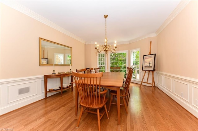 dining space with light wood-style floors, a notable chandelier, ornamental molding, and wainscoting