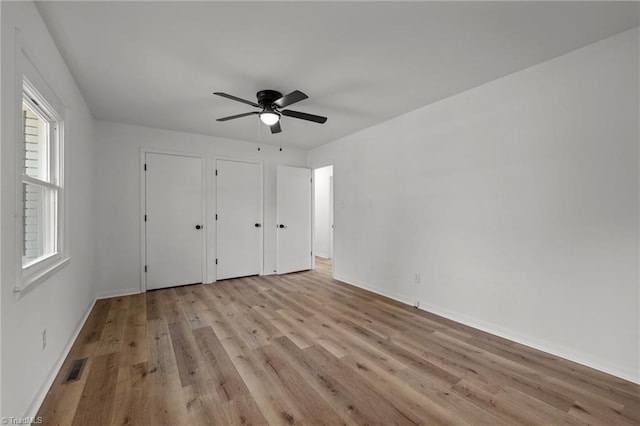 unfurnished bedroom featuring ceiling fan, light hardwood / wood-style floors, and two closets