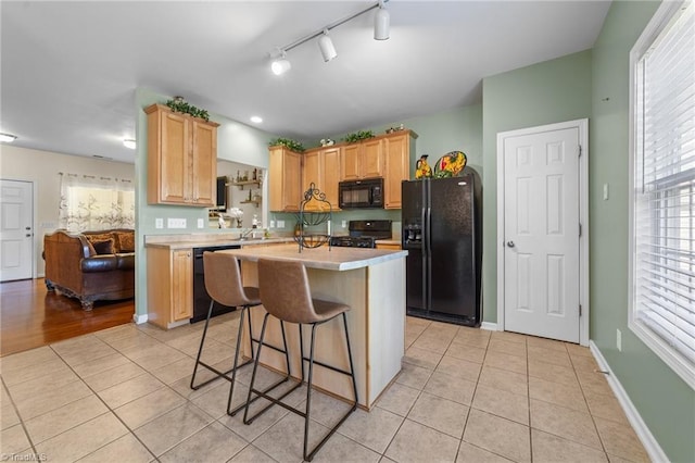 kitchen featuring light countertops, light brown cabinets, light tile patterned floors, and black appliances