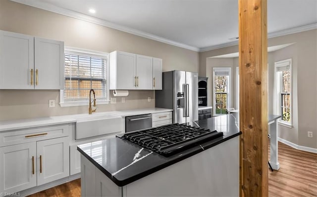 kitchen featuring a center island, ornamental molding, appliances with stainless steel finishes, wood finished floors, and a sink