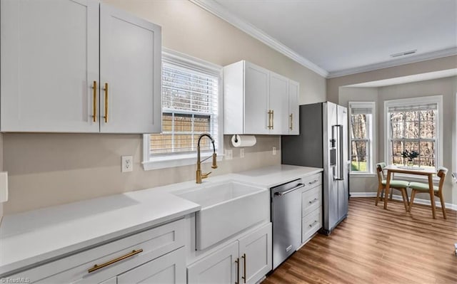 kitchen with ornamental molding, a sink, plenty of natural light, appliances with stainless steel finishes, and light countertops