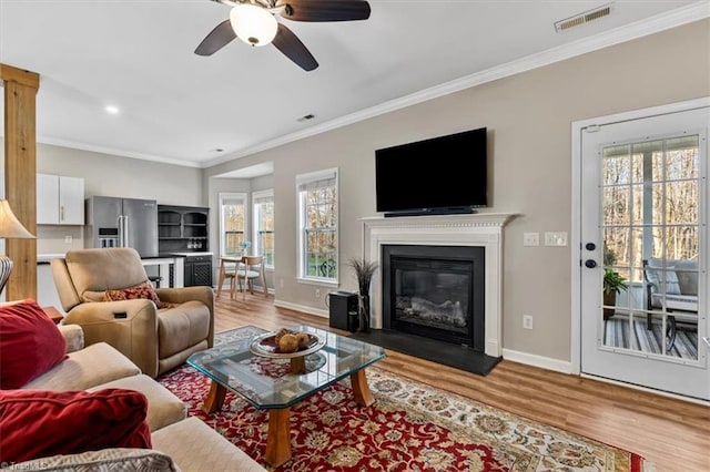 living room featuring visible vents, crown molding, a ceiling fan, and wood finished floors