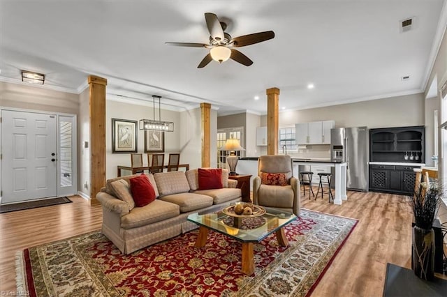 living area with light wood finished floors, visible vents, a ceiling fan, and decorative columns