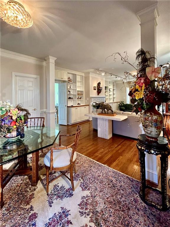 dining space featuring decorative columns, ornamental molding, dark wood-type flooring, built in features, and a notable chandelier