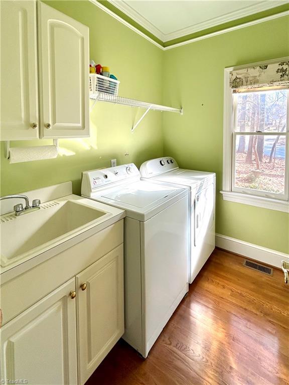 clothes washing area featuring sink, cabinets, light hardwood / wood-style floors, washer and dryer, and ornamental molding