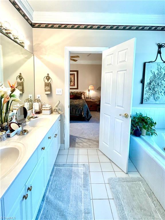 bathroom featuring tile patterned floors, vanity, a relaxing tiled tub, and ornamental molding