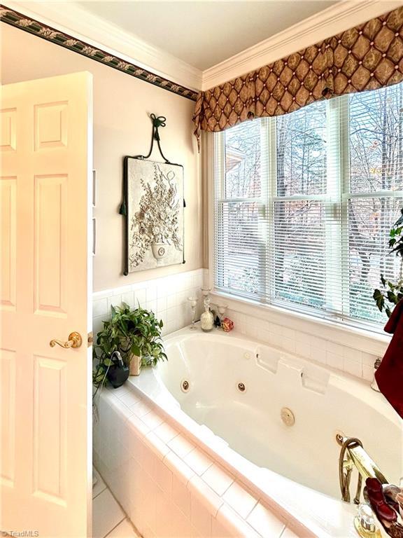 bathroom featuring ornamental molding, a relaxing tiled tub, and a healthy amount of sunlight