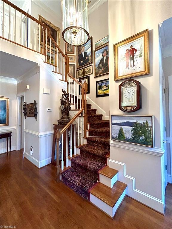 stairway with hardwood / wood-style floors, a towering ceiling, ornamental molding, and a notable chandelier