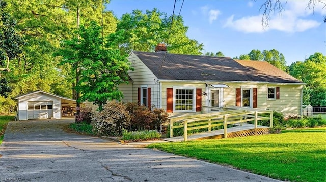 bungalow-style house featuring a front lawn, a chimney, an outbuilding, driveway, and a detached garage