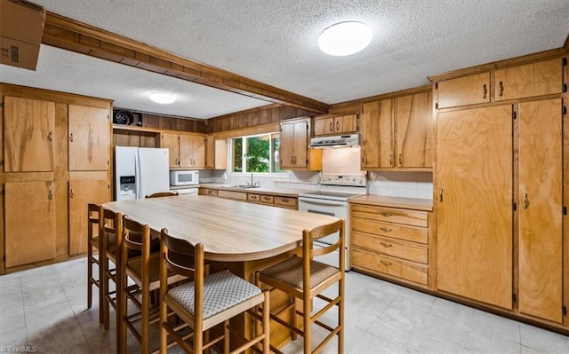 kitchen featuring a sink, white appliances, light countertops, a textured ceiling, and range hood