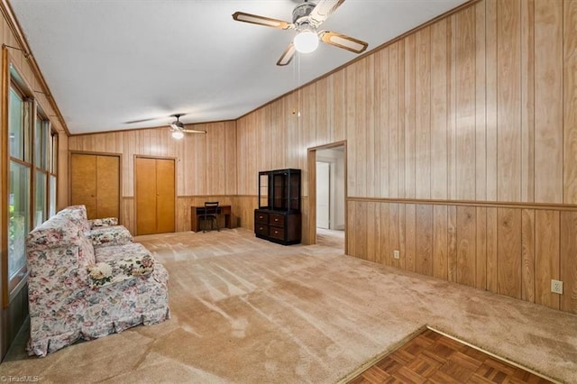 carpeted living room with a ceiling fan, vaulted ceiling, and wood walls