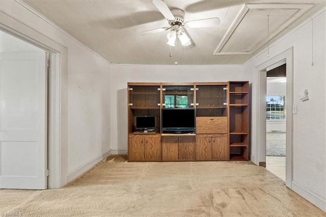 unfurnished living room featuring a ceiling fan, attic access, crown molding, carpet floors, and baseboards
