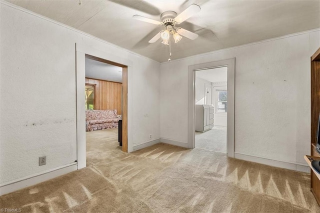 carpeted spare room featuring a ceiling fan, a textured wall, ornamental molding, and baseboards