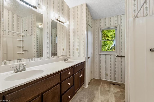 bathroom featuring a sink, a textured ceiling, and wallpapered walls
