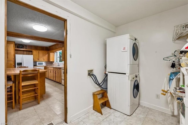 clothes washing area featuring laundry area, baseboards, stacked washing maching and dryer, a textured ceiling, and a sink