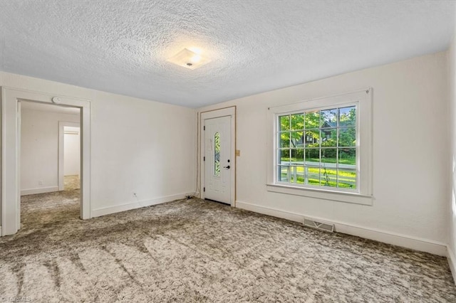 spare room with carpet flooring, a textured ceiling, visible vents, and baseboards