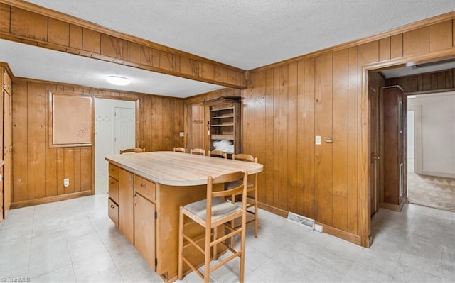 kitchen with light countertops, a textured ceiling, wood walls, baseboards, and visible vents