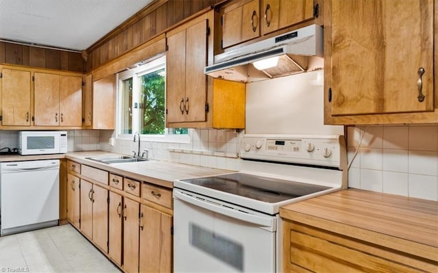 kitchen with a sink, backsplash, under cabinet range hood, and white appliances