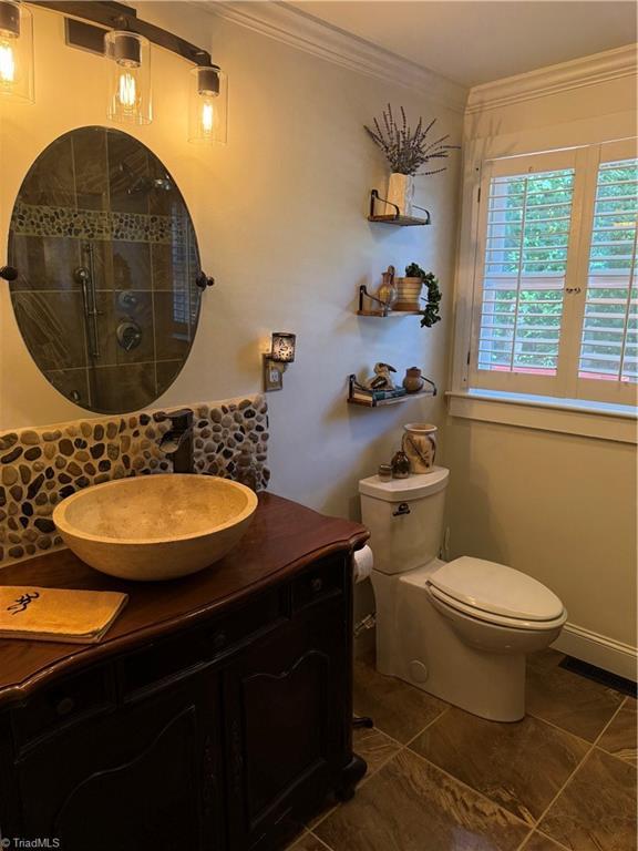 bathroom with ornamental molding, toilet, vanity, and tiled shower