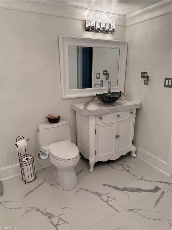 half bath with marble look tile flooring, crown molding, toilet, vanity, and baseboards