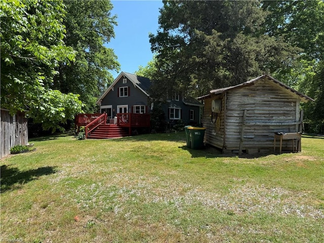 view of green lawn featuring a wooden deck and an outbuilding