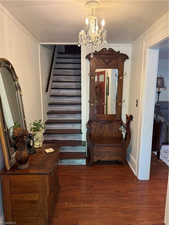 stairs with wood finished floors, a chandelier, ornamental molding, and baseboards