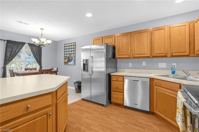 kitchen featuring sink, hanging light fixtures, a chandelier, appliances with stainless steel finishes, and light wood-type flooring