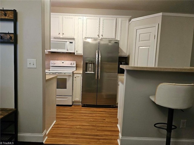 kitchen with white appliances, light wood-type flooring, a kitchen bar, white cabinetry, and crown molding