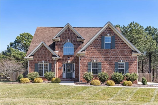 traditional-style home featuring brick siding, a front lawn, and fence