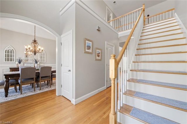 stairway featuring wood finished floors, a towering ceiling, arched walkways, baseboards, and a chandelier