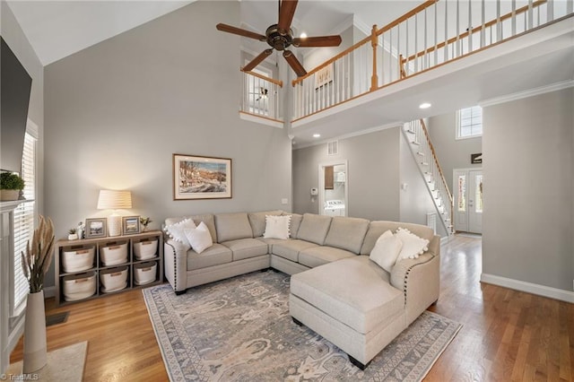 living room featuring stairs, baseboards, light wood finished floors, and high vaulted ceiling