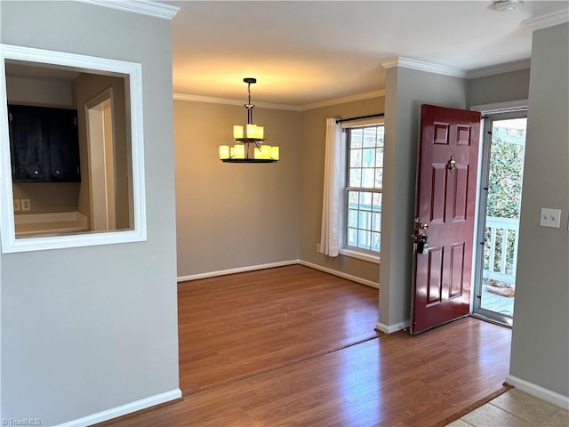 foyer entrance featuring baseboards, a notable chandelier, wood finished floors, and crown molding