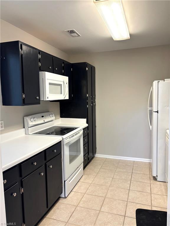 kitchen featuring white appliances, visible vents, light countertops, dark cabinetry, and light tile patterned flooring