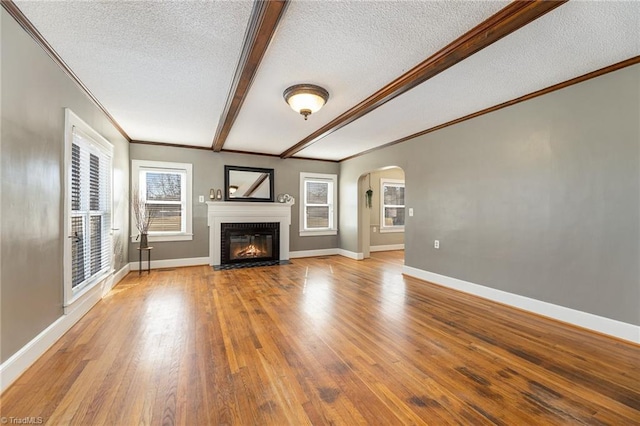 unfurnished living room with crown molding, hardwood / wood-style flooring, beam ceiling, a textured ceiling, and a brick fireplace