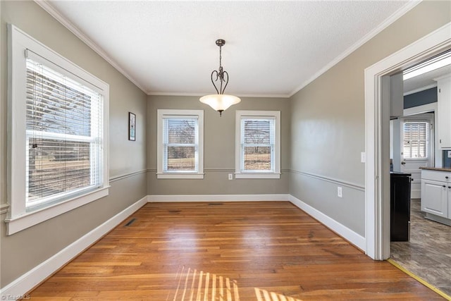 unfurnished dining area featuring hardwood / wood-style floors, a wealth of natural light, and ornamental molding