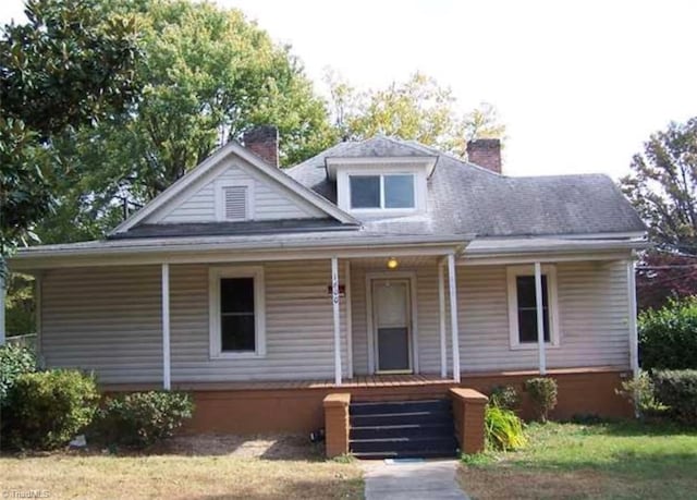view of front facade featuring a porch, a chimney, and a shingled roof