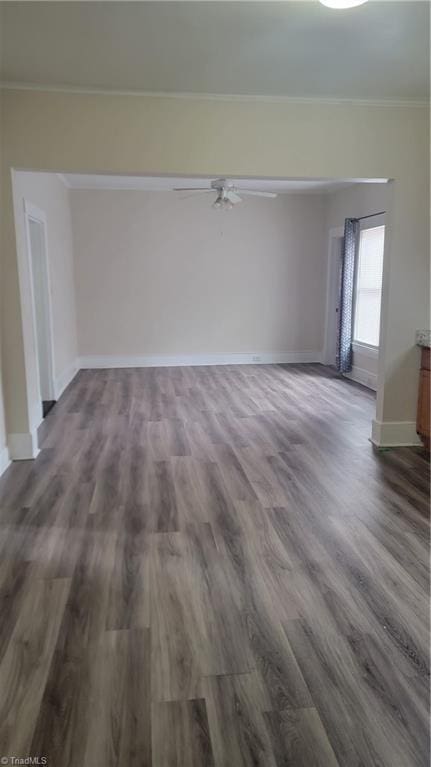 empty room featuring ornamental molding, baseboards, a ceiling fan, and dark wood-style flooring