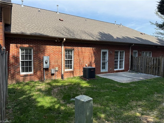 back of house featuring a shingled roof, fence, central air condition unit, a lawn, and a patio area