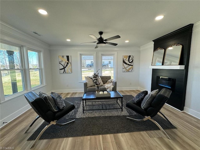 living room featuring a large fireplace, light hardwood / wood-style floors, ceiling fan, and crown molding