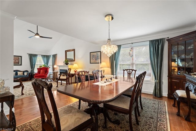 dining room featuring ceiling fan with notable chandelier, wood finished floors, and vaulted ceiling